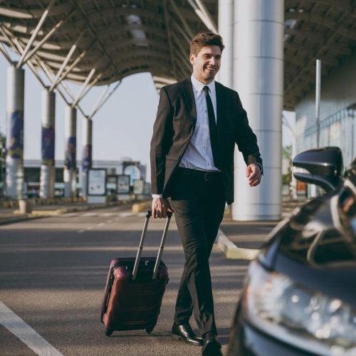 full body bottom view young traveler businessman young man in black dinner suit going walk outside at international airport terminal with suitcase to car booking taxi air flight business trip concept